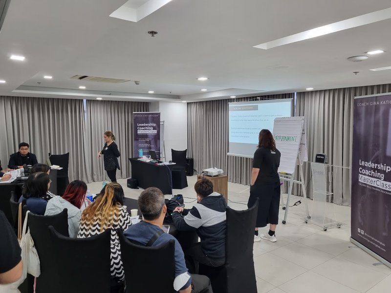 Coach Gina Katigbak leads a flipchart demonstration between two Leadership Coaching MasterClass banners.