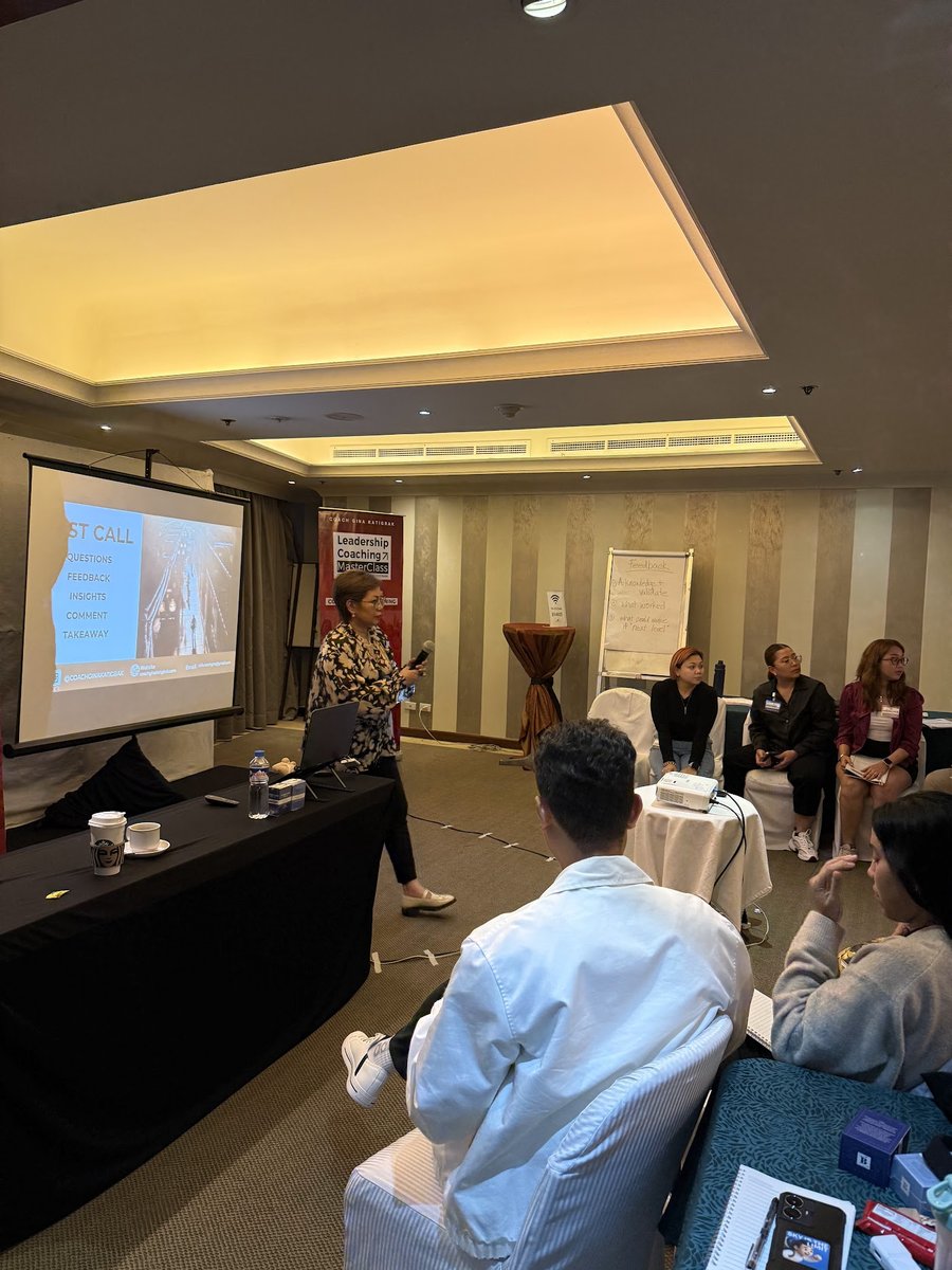 Coach Gina Katigbak teaches with a microphone beside her Leadership Coaching MasterClass banner during a live workshop.